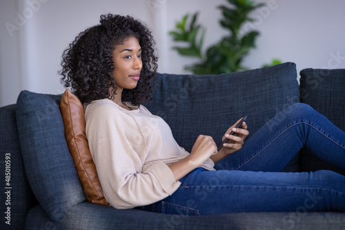 Young black woman at home sitting on a couch using cell phone texting