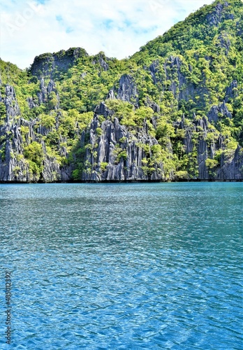 A limestone rock mountain is covered in mosses and shrubbery. The huge lime rock formation serves as a beautiful backdrop to the pristine lagoon