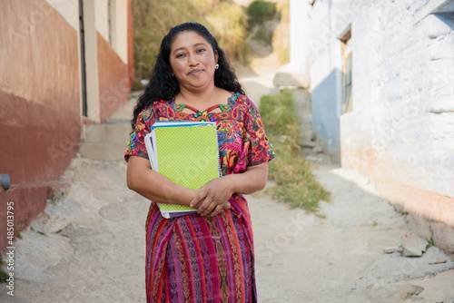 Hispanic mom with notebooks outside school in rural area - Mayan adult woman ready to go to study - Latina teacher in town