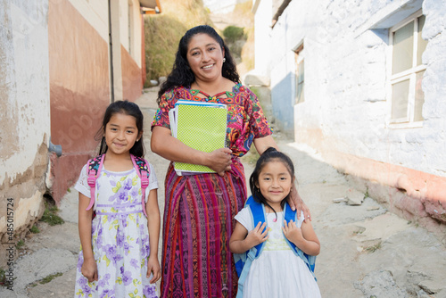 Hispanic mom and daughters ready to go to school - Latin mom accompanying her daughters to school - Hispanic girls with backpack outside their house in rural area photo