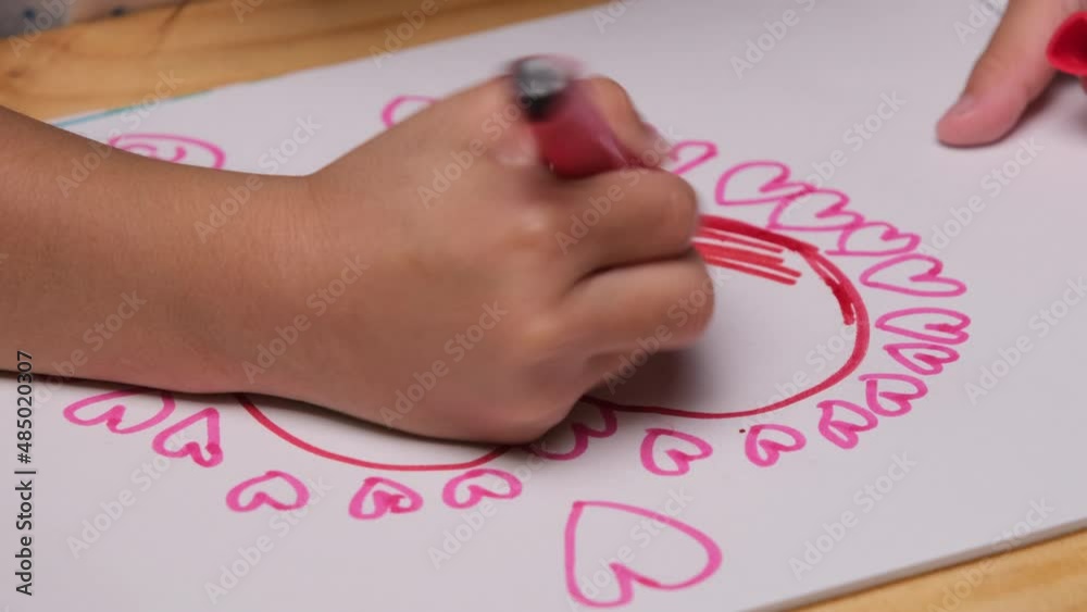 Close-up of a little girl drawing a heart and coloring with her colored markers. Cute young girl doing homework at table at home. Arts and crafts. Close-up of a little girl drawing a heart and coloring with her colored markers. Cute young girl doing homework at table at home. Arts and crafts.