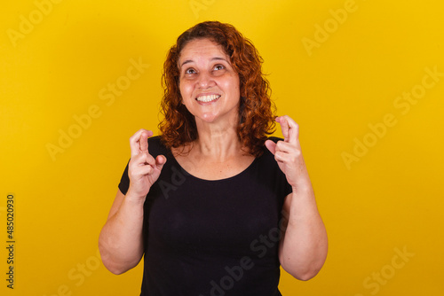 Foto Caucasian, Brazilian, Latin American woman, curly hair, curls, yellow background, sign of luck, luck, draw, fingers crossed, lottery, wishing, cheering