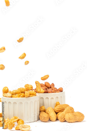 Varieties of peanuts in bowls with peanuts falling on white background