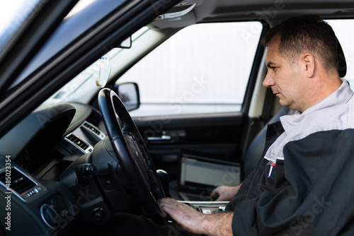 Professional auto mechanic sitting in a car and using laptop to check car diagnostics. © Dusan