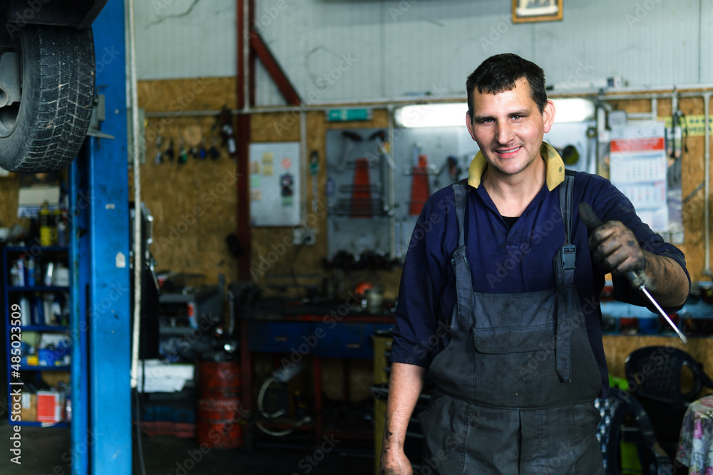 Portrait of auto mechanic in repair shop makes a gesture thumbs up. Portrait of auto mechanic in repair shop makes a gesture thumbs up.
