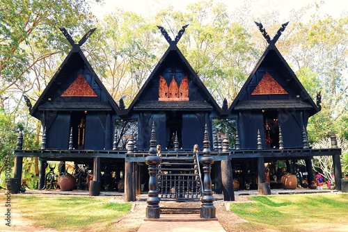 There are three black houses side by side in the forest of Baandam Museum photo