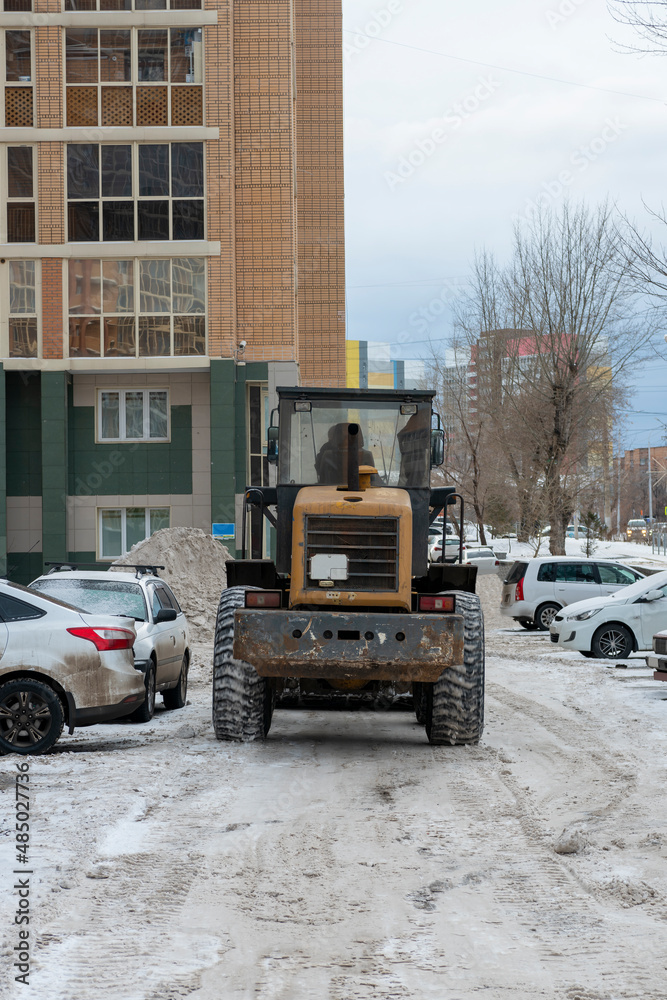 A tractor removes snow from the car park of a residential building.