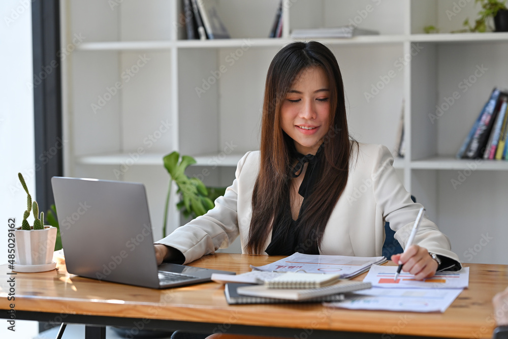 Asian businesswoman using laptop computer and writing information on document. Asian businesswoman using laptop computer and writing information on document.