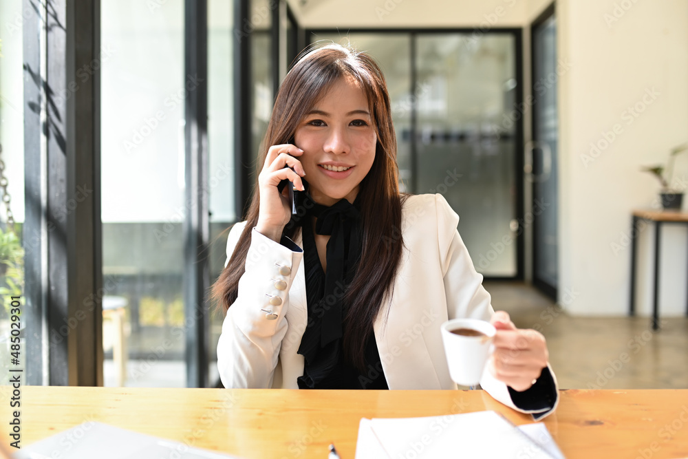 Pretty asian businesswoman holing coffee cup and talking on mobile phone. Pretty asian businesswoman holing coffee cup and talking on mobile phone.