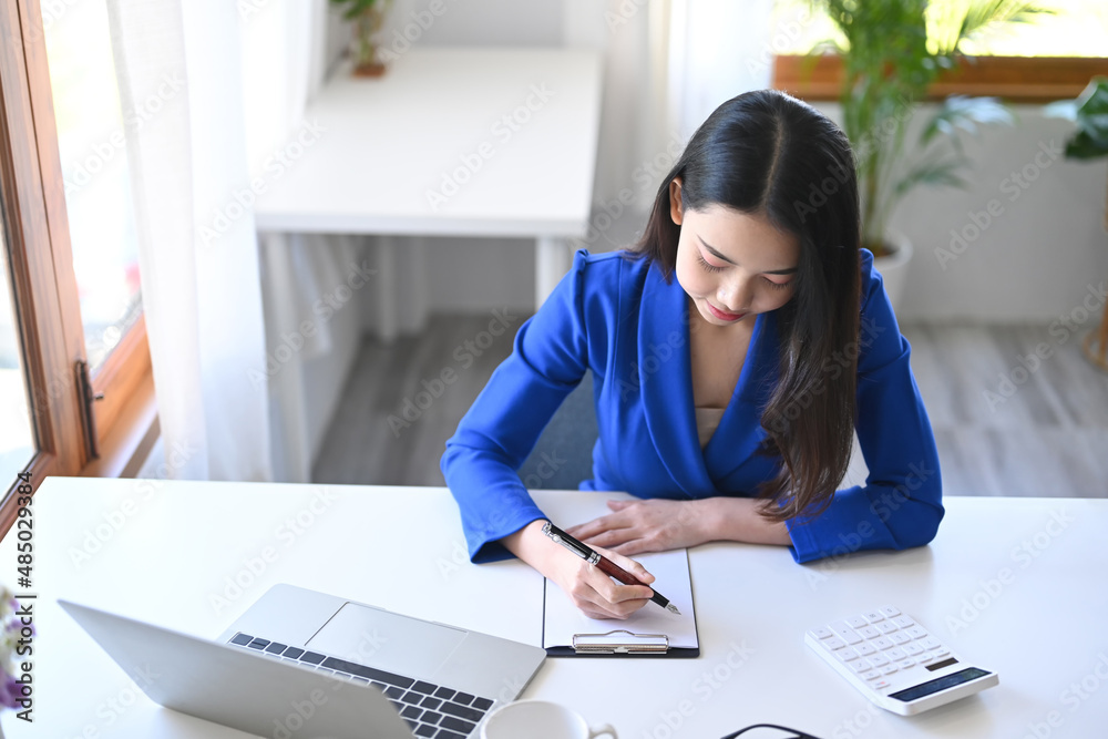 Young business woman working with laptop computer and making notes on notebook. Young business woman working with laptop computer and making notes on notebook.