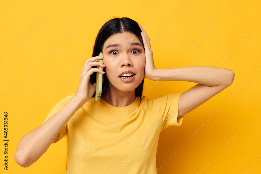 Portrait Asian beautiful young woman communicates on the phone emotions yellow background unaltered Portrait Asian beautiful young woman communicates on the phone emotions yellow background unaltered