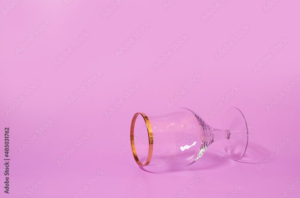 An empty wine glass lies on its side on a pink background