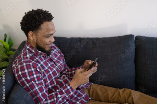 Black man at home sitting on a couch using texting on smart phone