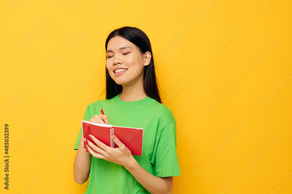 Charming young Asian woman green T-shirts with red notebook and pen isolated background unaltered Charming young Asian woman green T-shirts with red notebook and pen isolated background unaltered