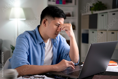Obraz na płótnie Young Asian man tired from hard work with eyes closed using hands to pinch and massage eyes and nose to relieve exhaustion and pain