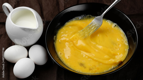 Scrambled eggs, omelette. Сhef whisking eggs in black bowl cooking omelette with milk. Traditional heathy breakfast