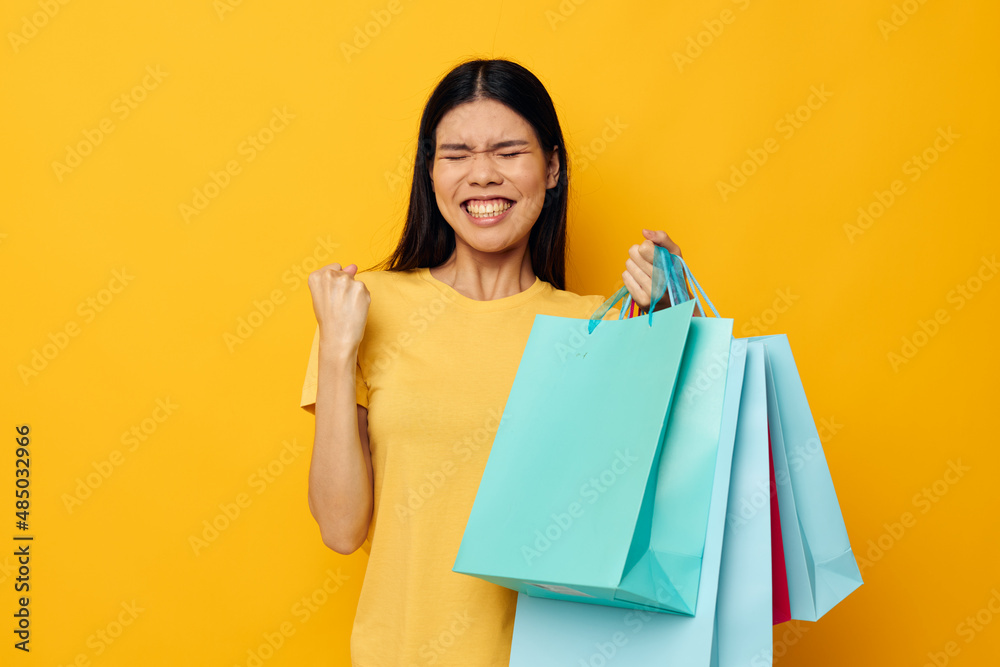woman with Asian appearance in a yellow T-shirt with multicolored shopping bags studio model unaltered woman with Asian appearance in a yellow T-shirt with multicolored shopping bags studio model unaltered
