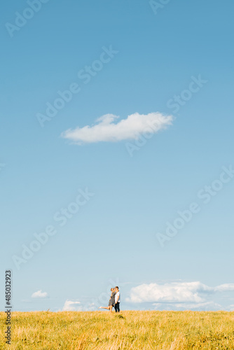 Loving couple kissing, flirting, hugging standing on horizon in meadow on sunny summer day against blue sky, young family enjoying each other, far view. Romantic trip, love story adventure concept © Sergio