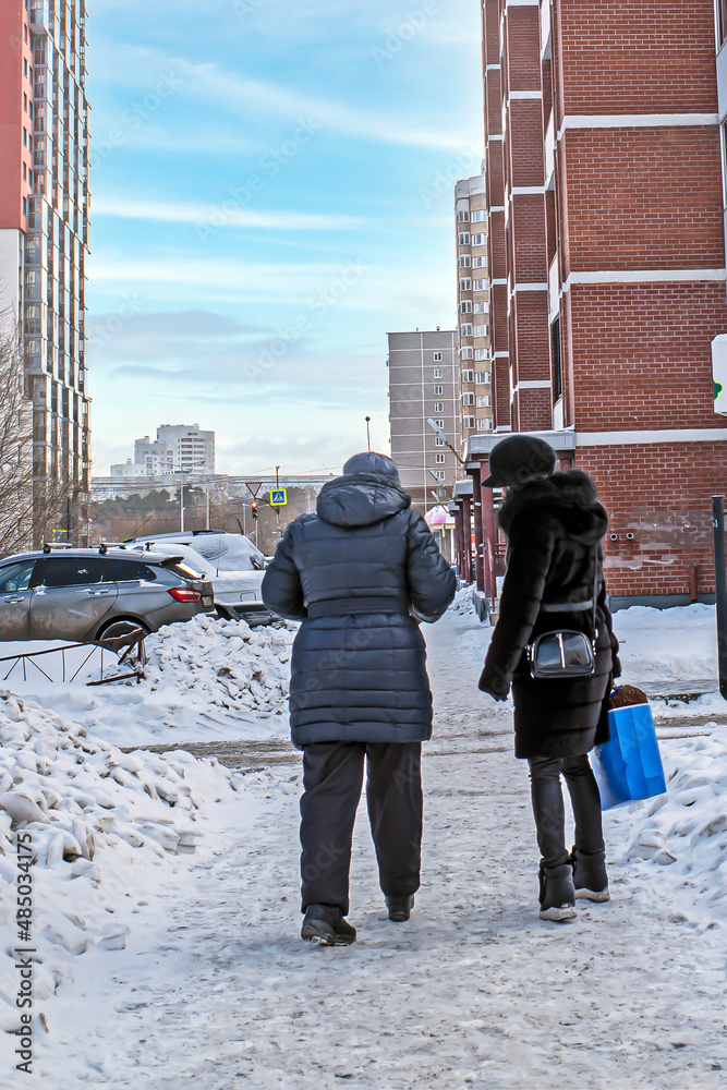Two women walk on a snowy sidewalk on a winter day
