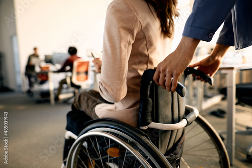 Close-up of colleague pushes businesswoman in wheelchair while arriving in the office.