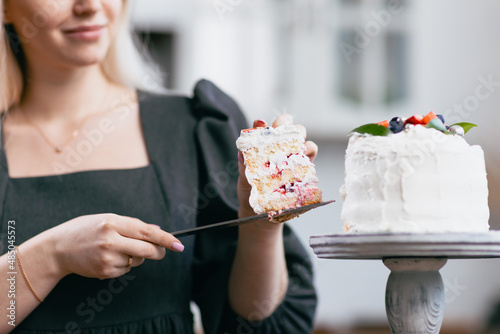 Pastry chef confectioner young caucasian woman in gray dress with knife cut slice cake on kitchen table. Cakes cupcakes and sweet dessert Scandinavian style