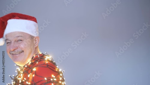 Senior bald man in christmas hat and garland waving hand welcoming friends.