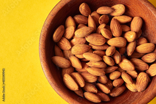 Almond nuts in a wooden bowl on a yellow background