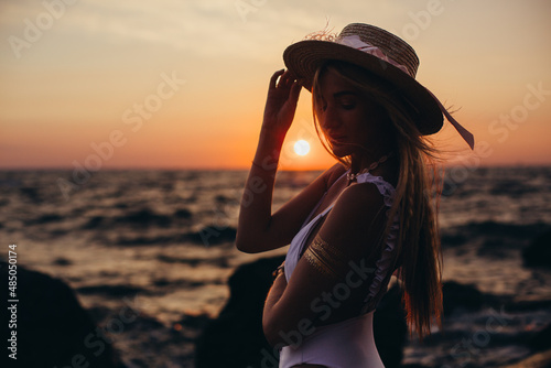 Silhouette of a girl in a hat on the background of the dawn sun close-up. Vacation, beach holiday concept.