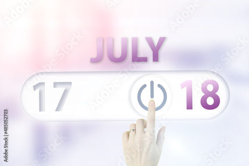 July 18th. Day 18 of month, Calendar date.Hand finger switches pointing calendar date on sunlight office background. Summer month, day of the year concept. photo