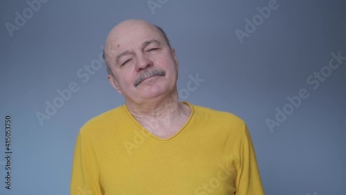 Tired senior man having pain or neck ache. Guy in casual yellow t-shirt takes break.