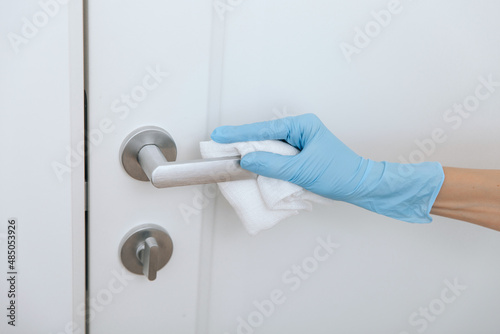 Cleaning black door handle with an antiseptic wet wipe in blue gloves. Woman hand using towel for cleaning. Sanitize surfaces prevention in hospital and public spaces against corona virus