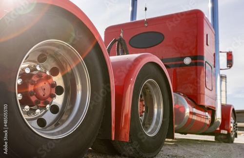 Classic red American semi truck in parking lot, detail of aluminum tandem axles with red hub caps. Low angle, rear view of big rig. Wide angle of powerful diesel US lorry.