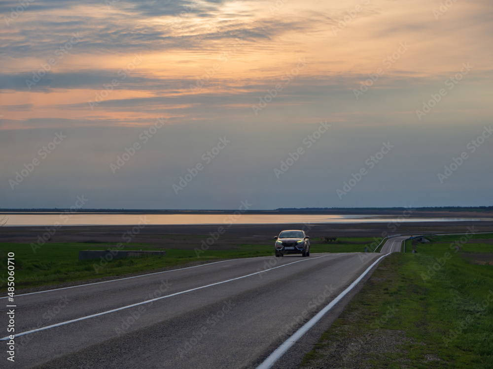 A car driving on the road in the countryside among nature at sunset. Paved road near the bay of the sea lagoon