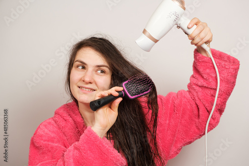 A beautiful woman combs her tangled hair with a comb and dries it with a hair dryer. photo