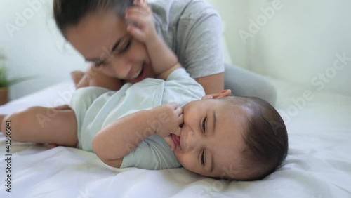 Happy mother playing with her baby lying together on bed