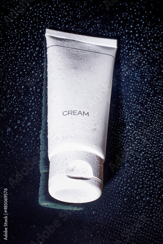 White bottles of cosmetics on a black background in water drops