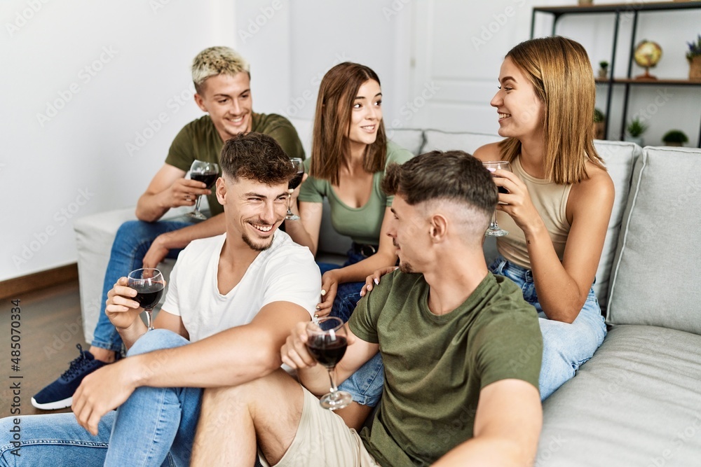 Group of young friends smiling happy drinking red wine at home.