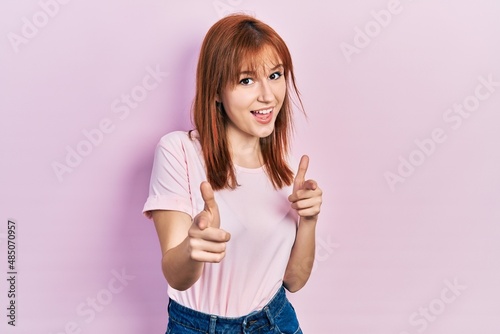 Redhead young woman wearing casual pink t shirt pointing fingers to camera with happy and funny face. good energy and vibes. © Krakenimages.com