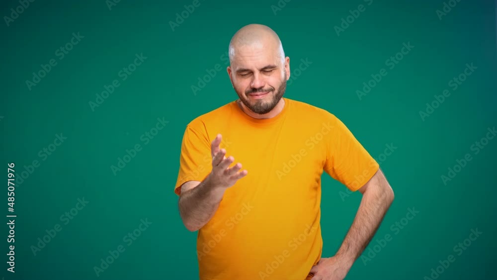 Bald middle-aged man with a beard in an orange t-shirt agrees nodding his head on a green background Bald middle-aged man with a beard in an orange t-shirt agrees nodding his head on a green background