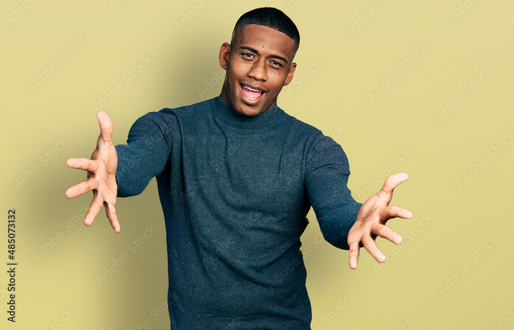 Young black man wearing casual sweater looking at the camera smiling with open arms for hug. cheerful expression embracing happiness. Young black man wearing casual sweater looking at the camera smiling with open arms for hug. cheerful expression embracing happiness.