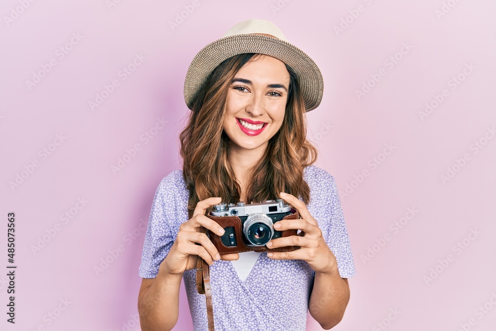 Young hispanic girl wearing summer hat holding vintage camera smiling with a happy and cool smile on face. showing teeth.