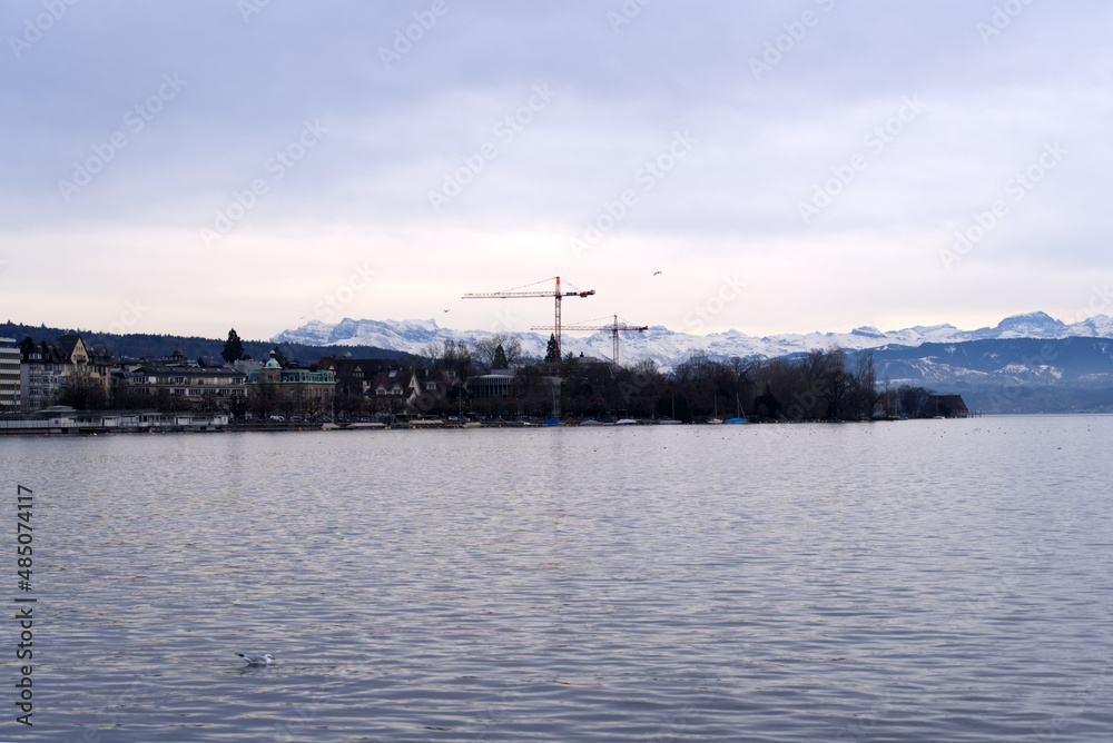 Beautiful scenic landscape with Lake Zurich in the foreground and Swiss Alps in the background on a cloudy winter afternoon. Photo taken February 3rd, 2022, Zurich, Switzerland.