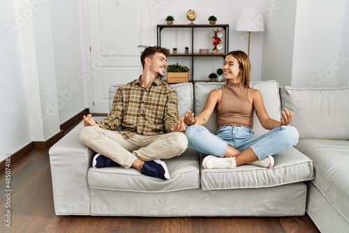 Young hispanic couple smiling happy doig yoga exercise sitting on the sofa at home. photo