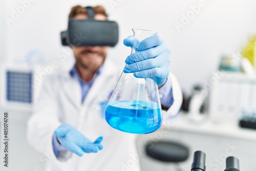 Middle age hispanic man wearing scientist uniform using vr glasses holding test tube at laboratory