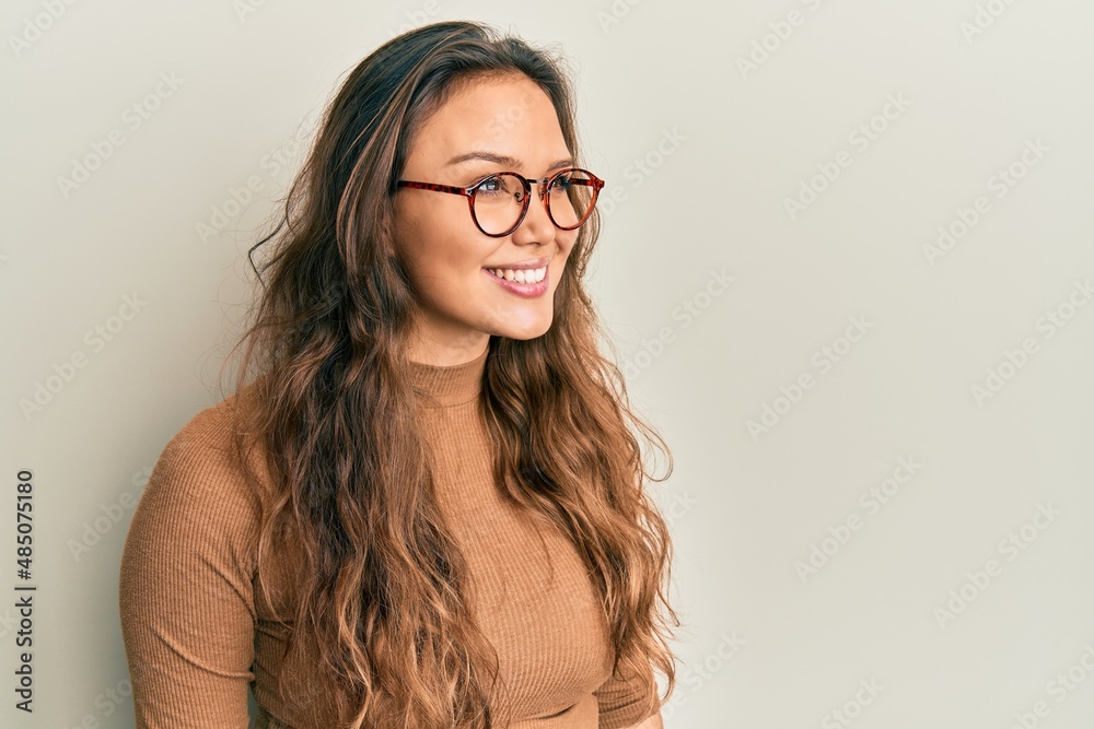 Young hispanic girl wearing casual clothes and glasses looking away to side with smile on face, natural expression. laughing confident.