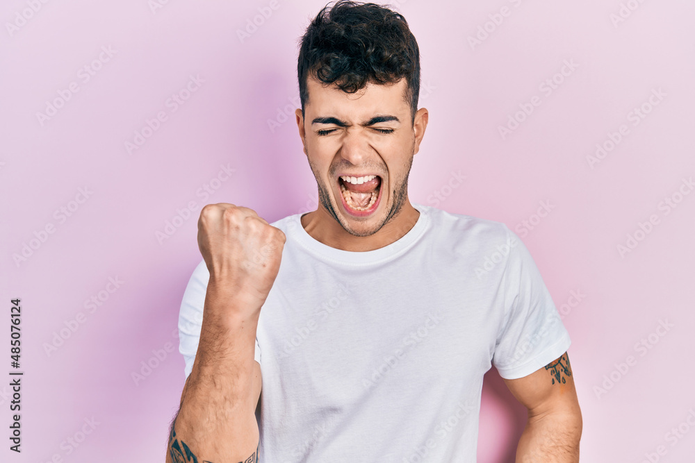Young hispanic man wearing casual white t shirt celebrating surprised and amazed for success with arms raised and eyes closed Young hispanic man wearing casual white t shirt celebrating surprised and amazed for success with arms raised and eyes closed