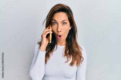 Young latin woman having conversation talking on the smartphone scared and amazed with open mouth for surprise, disbelief face