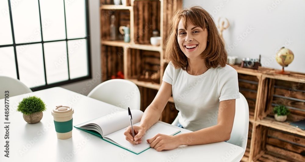 Young caucasian woman writing on notebook sitting on table at home Young caucasian woman writing on notebook sitting on table at home