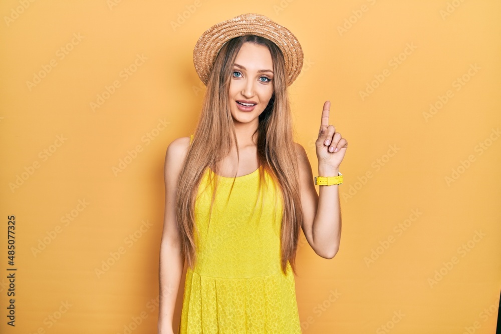 Young blonde girl wearing summer hat pointing finger up with successful idea. exited and happy. number one. Young blonde girl wearing summer hat pointing finger up with successful idea. exited and happy. number one.