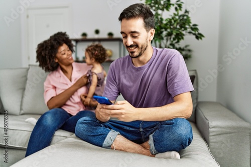 Couple and daughter using smartphone sitting on sofa at home